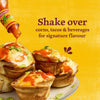 A bottle of Cholula Original Mexican Hot Sauce 150Ml is being drizzled over a stack of savory breakfast egg cups topped with green onions against a bright yellow background.
