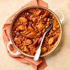 An overhead shot of a hearty sausage and bean casserole in a white enameled pot with a serving spoon.
