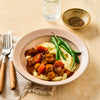 A comforting meal of beef stew with carrots and mushrooms is served over creamy mashed potatoes with a side of green beans, with a small bowl of cracked black pepper nearby.