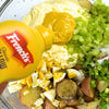 A bottle of Frenchs Classic Yellow Mustard is squeezed into a bowl of potato salad ingredients as part of the Global Visionary Template Uk.