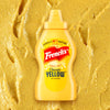 A bottle of Frenchs Classic Yellow Mustard belonging to the Global Visionary Template Uk is centered against a textured background of spread yellow mustard.