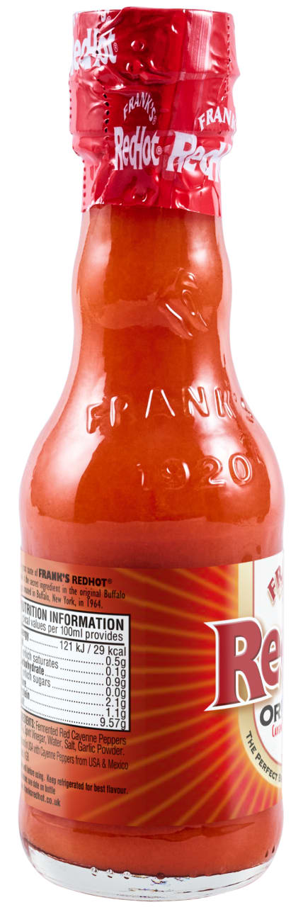 A glass bottle of Franks Rdhot Orig Gb 24/148 Ml is shown from the back, displaying the nutrition label and the embossed Frank's 1920 logo on the glass.