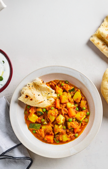 Bowl of vegetable curry with naan bread on a light background