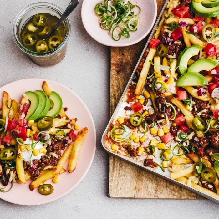A delicious tray of loaded fries is topped with a savory chili made using Schwartz Hot Chilli Con Carne Recipe Mix 41G, alongside fresh avocado, jalapeños, and corn.