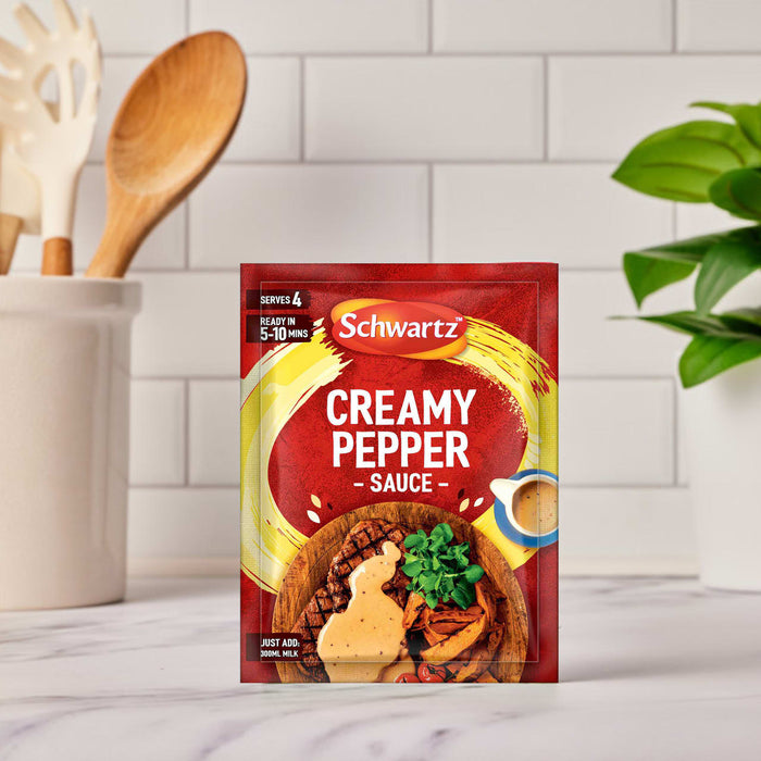 A packet of Schwartz Creamy Pepper Sauce Mix 25G is displayed on a white marble kitchen counter, ready to be prepared.