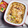 A freshly baked chicken and leek casserole with a golden-brown cheesy topping is presented in a white and red baking dish, next to the packet of Schwartz Chicken Casserole Recipe Mix 36G used to prepare the meal.