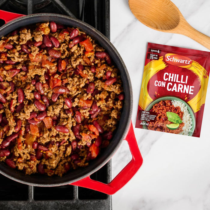 A red pot filled with freshly made chilli con carne sits on a stovetop, with a packet of Schwartz Chilli Con Carne Recipe Mix 41G and a wooden spoon resting on the counter beside it.
