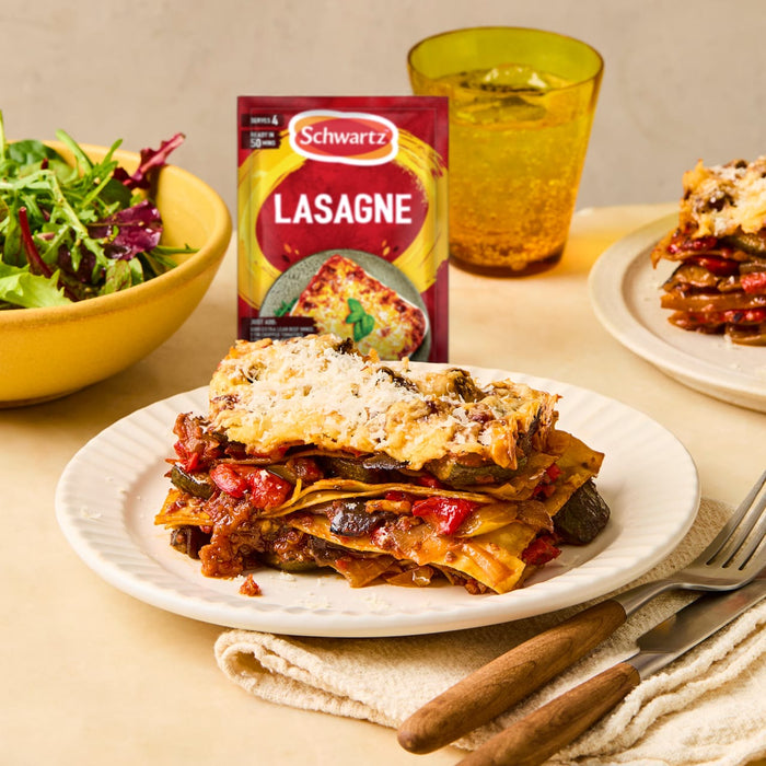A plated slice of vegetable lasagne sits next to a side salad, with a packet of Schwartz Lasagne Recipe Mix 36G in the background, suggesting a delicious meal idea.