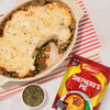 A delicious-looking Shepherd's Pie in a baking dish, with a scoop taken out, sits next to the packet of Schwartz Shepherd'S Pie Recipe Mix 38G that helps create the meal.