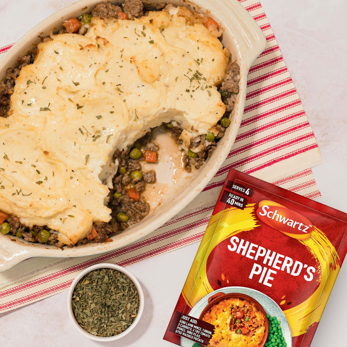 A delicious-looking Shepherd's Pie in a baking dish, with a scoop taken out, sits next to the packet of Schwartz Shepherd'S Pie Recipe Mix 38G that helps create the meal.