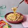A delicious bowl of spaghetti carbonara, made using a packet of Schwartz Spaghetti Carbonara Recipe Mix 32G, is being twirled on a fork next to a glass of sparkling water.