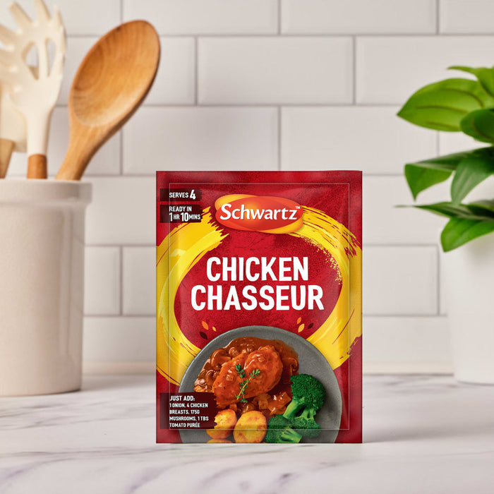 A packet of Schwartz Chicken Chasseur Recipe Mix 40G is displayed on a marble countertop in a bright kitchen setting with cooking utensils and a plant in the background.