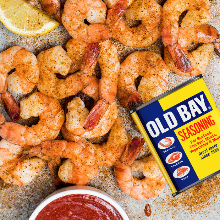 A platter of seasoned shrimp and a lemon wedge are served with cocktail sauce and a tin of Old Bay Seasoning.