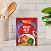 A packet of Schwartz Roast Beef Gravy Mix 27G is displayed on a marble kitchen counter, with a utensil holder and a green plant blurred in the background.