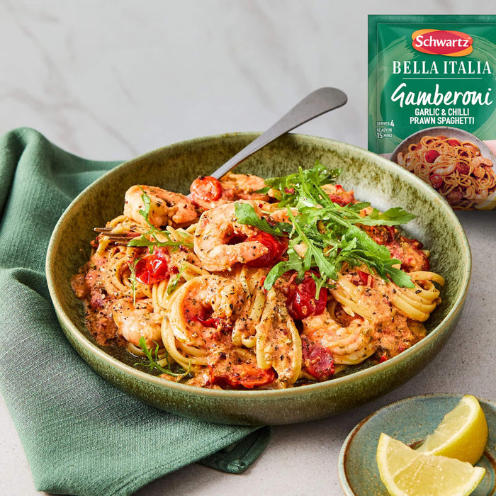 A rustic green bowl holds a creamy serving of prawn and tomato spaghetti, garnished with fresh rocket, presented alongside the green packet of Schwartz Bella Italia Gamberoni Garlic & Chilli Prawn Spaghetti 35G.