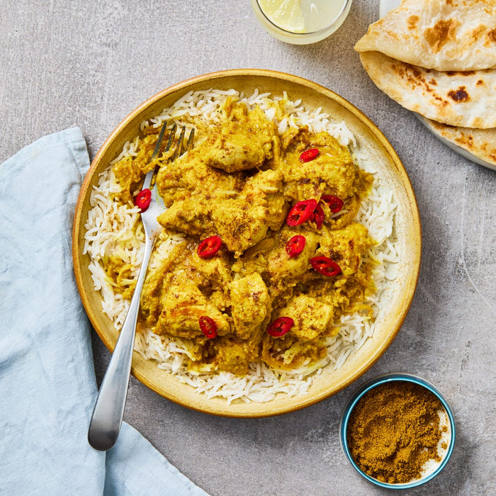 A delicious-looking bowl of chicken curry served over rice, a meal that can be made using Schwartz Las Iguanas Bahian Coconut Curry 25G, is pictured alongside flatbread and a refreshing drink.