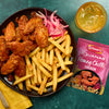 A plate of crispy fries and chicken wings coated in a sweet and spicy glaze is presented alongside a packet of Schwartz Las Iguanas Honey Chilli Chicken 35G and a refreshing iced drink.