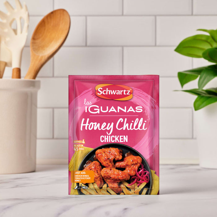 A packet of Schwartz Las Iguanas Honey Chilli Chicken 35G seasoning mix stands on a marble countertop in a bright kitchen setting.