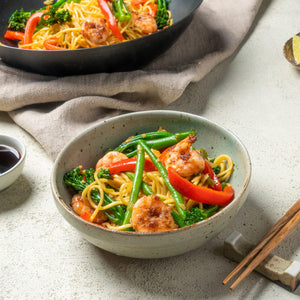 A vibrant shrimp and vegetable stir fry served in a ceramic bowl and a black wok is seasoned with Schwartz Chinese 5 Spice Seasoning 58G for an authentic flavor.