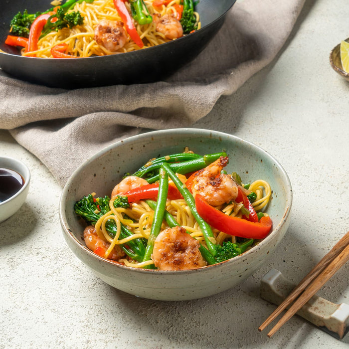 A vibrant shrimp and vegetable stir fry served in a ceramic bowl and a black wok is seasoned with Schwartz Chinese 5 Spice Seasoning 58G for an authentic flavor.