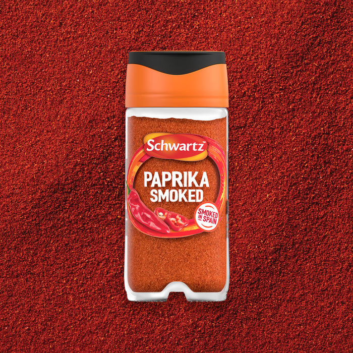 A clear jar of Schwartz Smoked Paprika 40G is centered in a product shot, resting on a bed of the same vibrant red spice to showcase its color and texture.