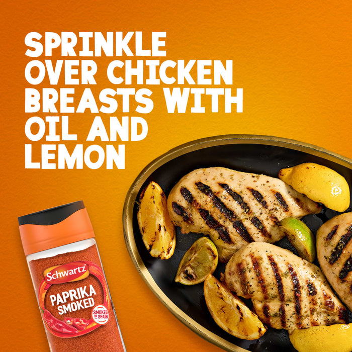 A bottle of Schwartz Smoked Paprika 40G is shown next to a black dish of grilled chicken breasts and lemon wedges on an orange background.