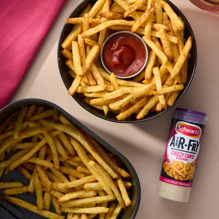 A container of Schwartz Af Fries Seas sits next to two bowls of golden air-fried chips served with a side of ketchup.