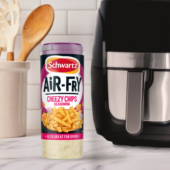 A container of Schwartz Af Fries Seas Cheezy Chips Seasoning stands on a marble countertop next to a black air fryer in a bright kitchen setting.