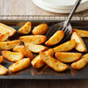 Golden brown potato wedges are seasoned with Schwartz Af Fries Seas and served on a baking sheet with a metal spatula.