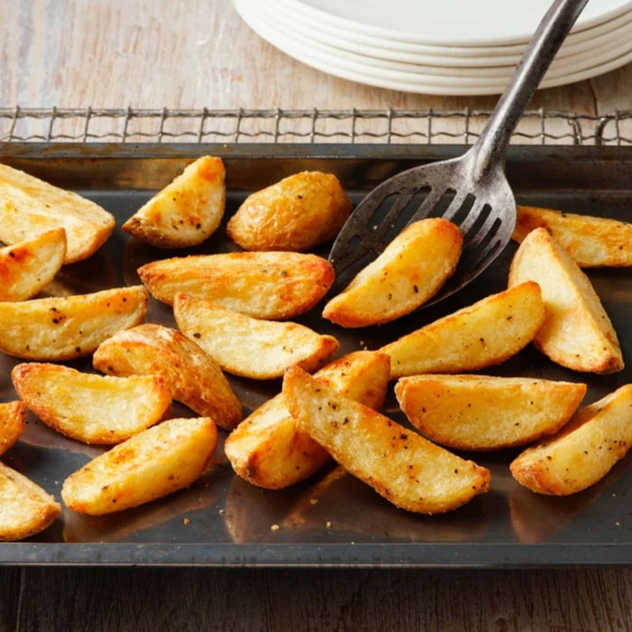 Golden brown potato wedges are seasoned with Schwartz Af Fries Seas and served on a baking sheet with a metal spatula.