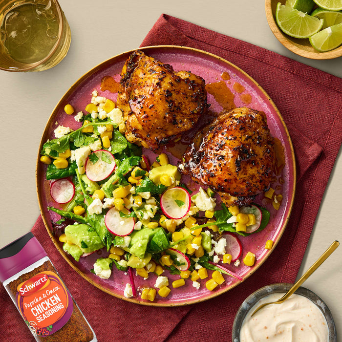 Two roasted chicken thighs seasoned with Schwartz Paprika and Onion Chicken Seasoning 50G are served on a pink plate alongside a vibrant corn and avocado salad.