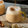 A warm, frothy beverage in a ribbed glass mug is garnished with a dusting of Schwartz Ground Cinnamon 39G, adding a final touch of flavor.