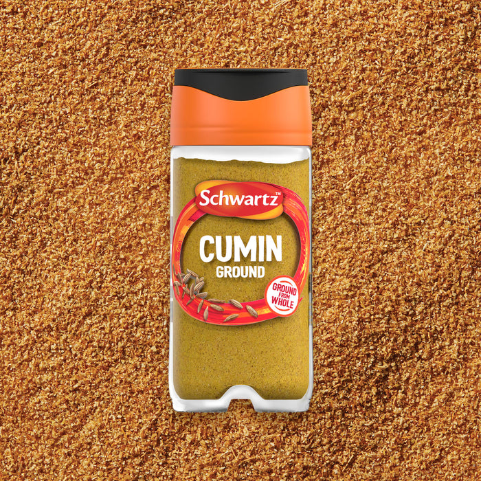 A clear jar of Schwartz Cumin Ground 37G is centered on a textured background of the ground spice.