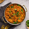 A delicious bowl of lentil and spinach curry is served in a metal karahi, garnished with fresh cilantro and a sprinkle of Schwartz Cumin Ground 37G.