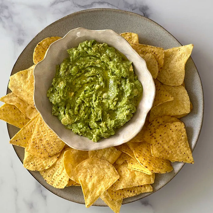 A rustic bowl of freshly made guacamole, perfectly seasoned with Schwartz Garlic Granules 50G, is presented on a platter surrounded by tortilla chips.