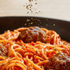 Dried Schwartz Mixed Herbs 11G are sprinkled over a bowl of spaghetti and meatballs in a rich tomato sauce.