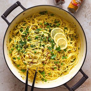 A large pot of vibrant yellow spaghetti with peas and lemon is shown as a delicious meal idea using Schwartz Turmeric Ground 37G, with the spice jar visible in the background.