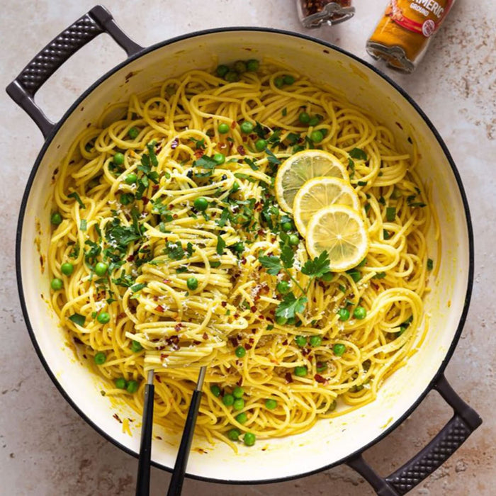 A large pot of vibrant yellow spaghetti with peas and lemon is shown as a delicious meal idea using Schwartz Turmeric Ground 37G, with the spice jar visible in the background.