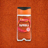 A clear glass jar of Schwartz Paprika 40G is centered on a background of the same vibrant red spice.