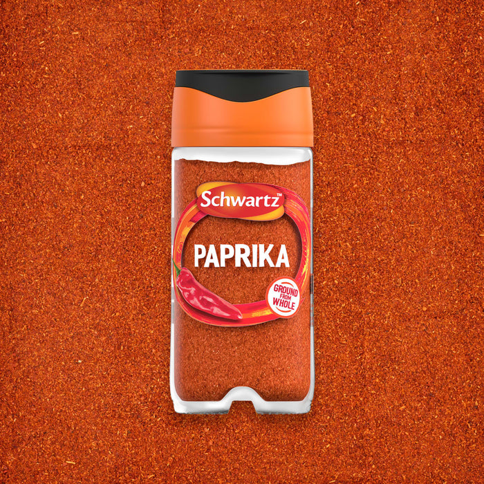 A clear glass jar of Schwartz Paprika 40G is centered on a background of the same vibrant red spice.