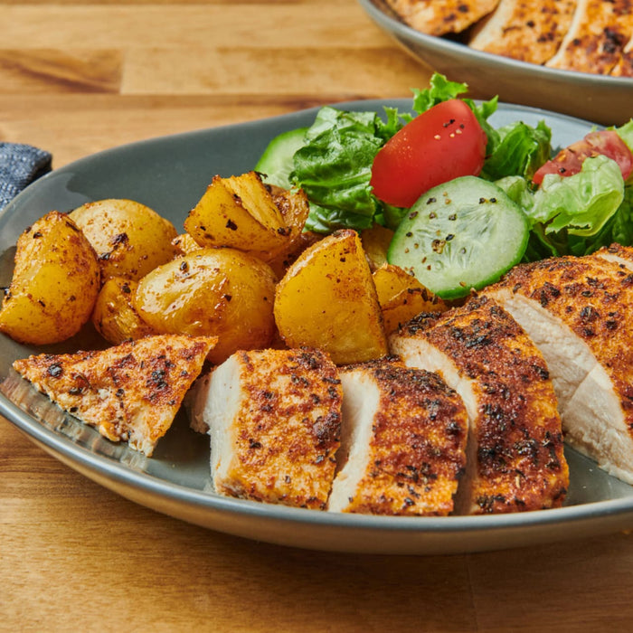 A delicious plate of sliced chicken and roasted potatoes, seasoned to perfection with Schwartz Onion Granules 30G, is served alongside a fresh side salad.