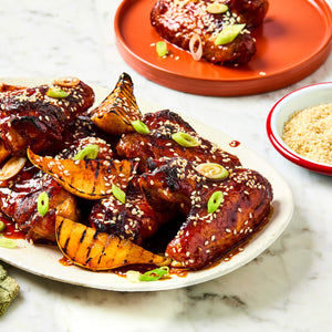 A platter of glazed chicken wings and grilled pear wedges seasoned with Schwartz Af Sy Korean Seas and garnished with sesame seeds and sliced green onions.