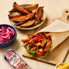 A vibrant meal featuring a wrap filled with seasoned meat and peppers alongside sweet potato wedges and pickled onions, all flavored with Schwartz Af Turki Keb Seas.
