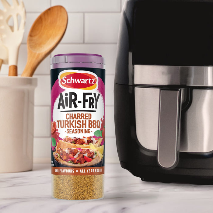 A container of Schwartz Af Turki Keb Seas stands on a marble countertop next to a black air fryer and a jar of wooden cooking utensils