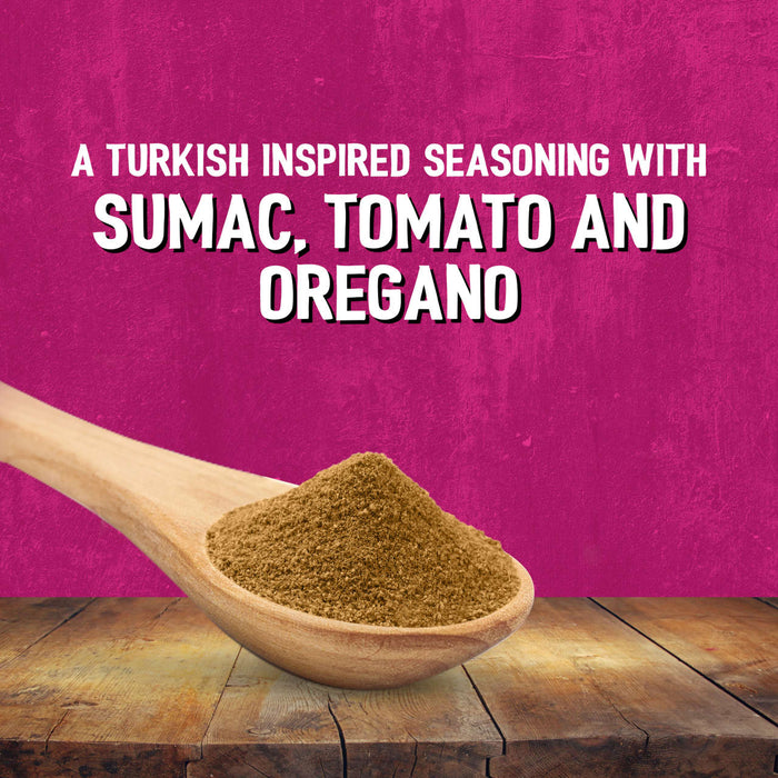A wooden spoon holds a mound of Schwartz Af Turki Keb Seas against a textured pink background with text describing it as a Turkish inspired seasoning with sumac tomato and oregano.