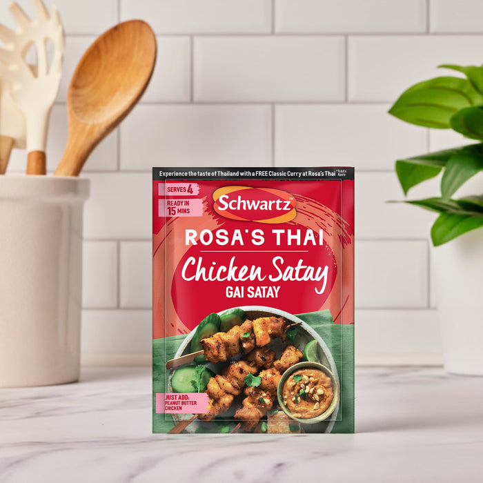 A packet of the Sa Rt Chicken Satay X12 seasoning mix from Schwartz is displayed on a kitchen counter next to a finished dish of chicken satay skewers and peanut sauce.