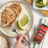 An overhead shot shows a bowl of sliced chicken over rice, with a hand holding a fork, next to a jar of Schwartz Crushed Chillies 29G, suggesting a spicy and flavorful meal.