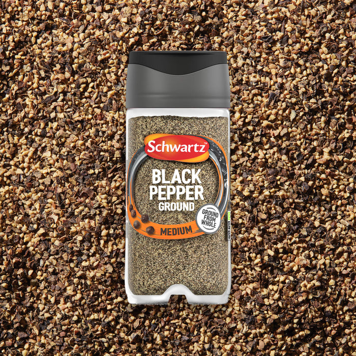 A clear plastic container of Schwartz Ground Black Pepper, 33G, is shown centered on a bed of coarse ground black pepper.