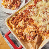 A delicious-looking pasta bake in a red dish, seasoned with Schwartz Ground Black Pepper, 33G, is being served onto a plate.