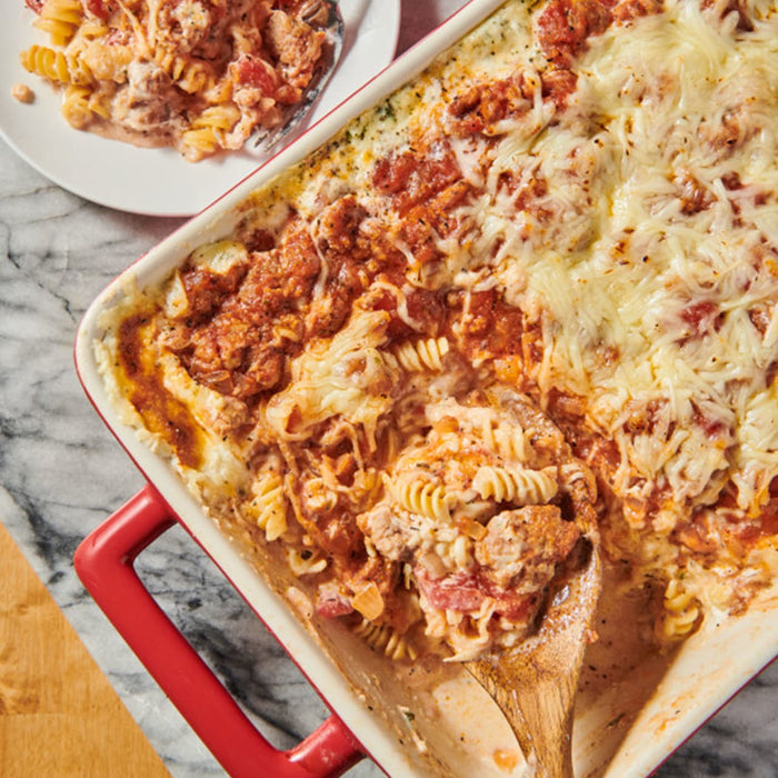 A delicious-looking pasta bake in a red dish, seasoned with Schwartz Ground Black Pepper, 33G, is being served onto a plate.